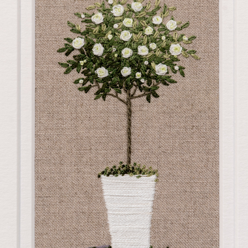 Hand embroidered artwork of a white standard rose in a white pot on beige linen background