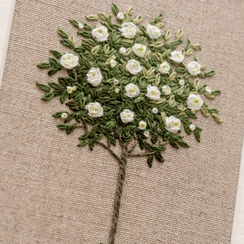 close up of the detail in this hand embroidered white standard rose on beige linen
