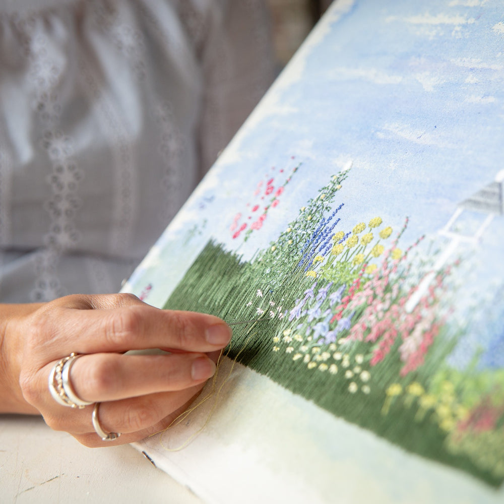 angled close up of Jo's hand embroidering daisies onto the Cottage Garden embroidery artwork.