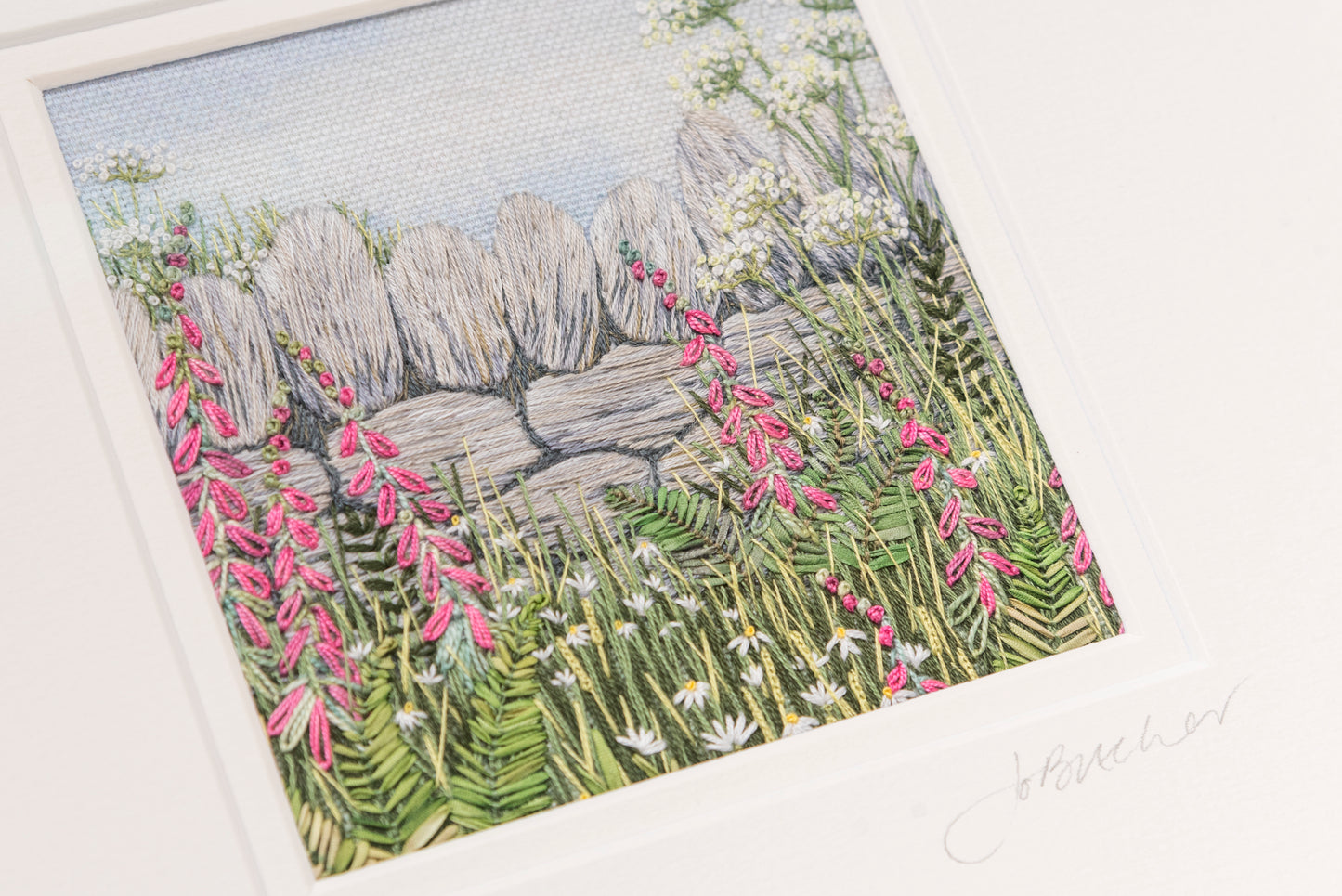 hand embroidery artwork of a dry stone wall with pink foxgloves, ferns, daisy and grasses in front in a white mount signed by Jo_Butcher